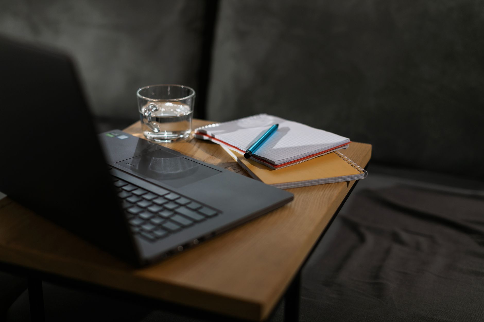 Un espace de travail minimaliste avec un ordinateur portable, des carnets et un verre d'eau sur une table en bois.