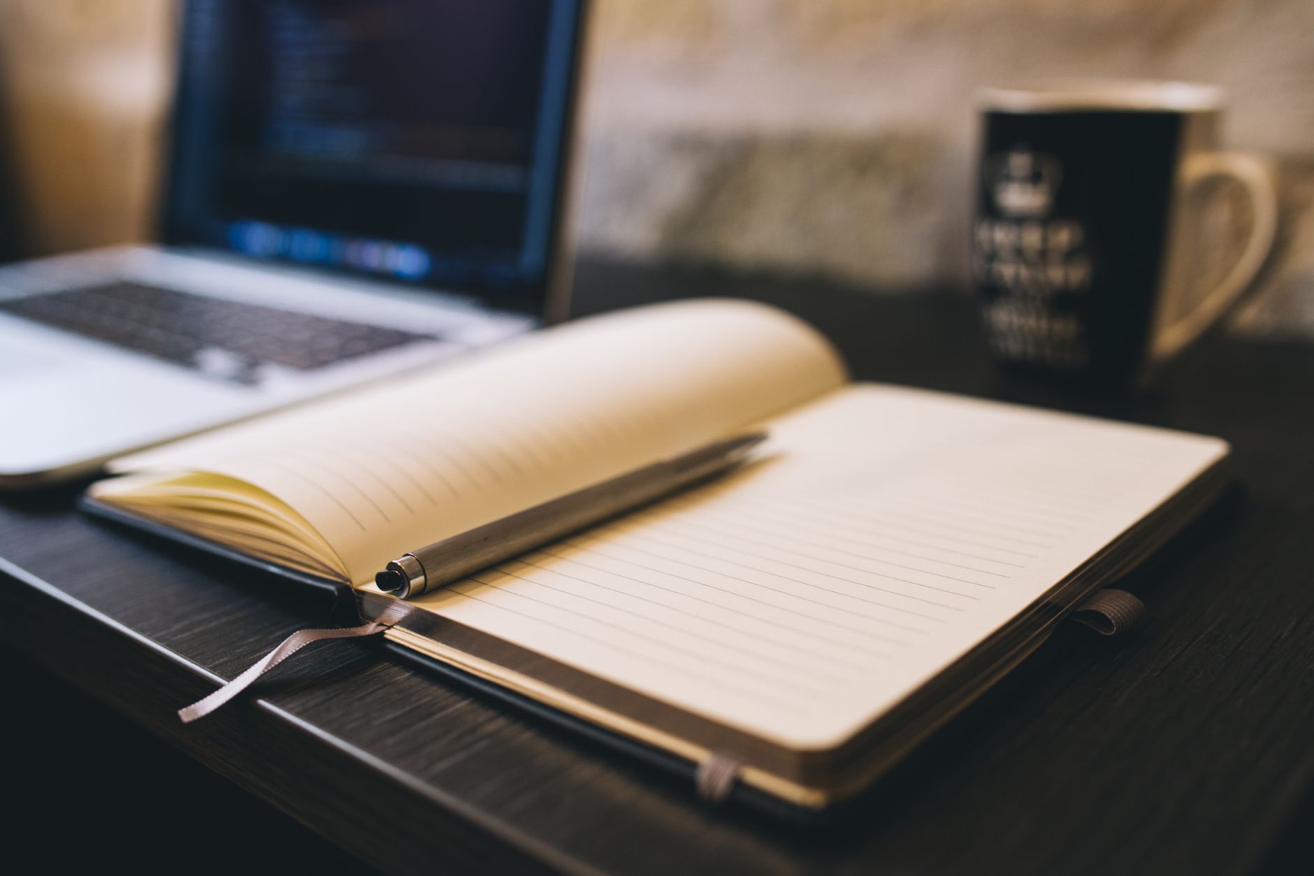 Carnet ouvert avec un stylo sur un bureau en bois, à côté d'un ordinateur portable, illustrant le travail rédactionnel.