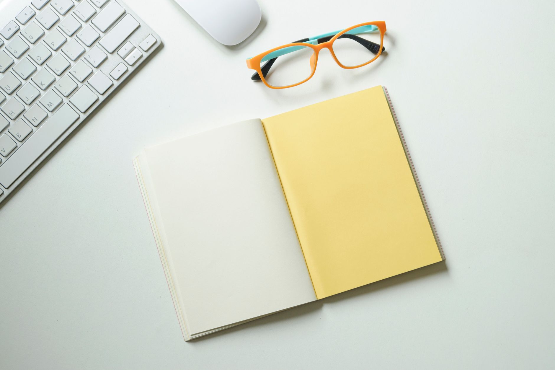 Vue de dessus d'un espace de travail propre avec un clavier, une souris, des lunettes et un carnet ouvert.